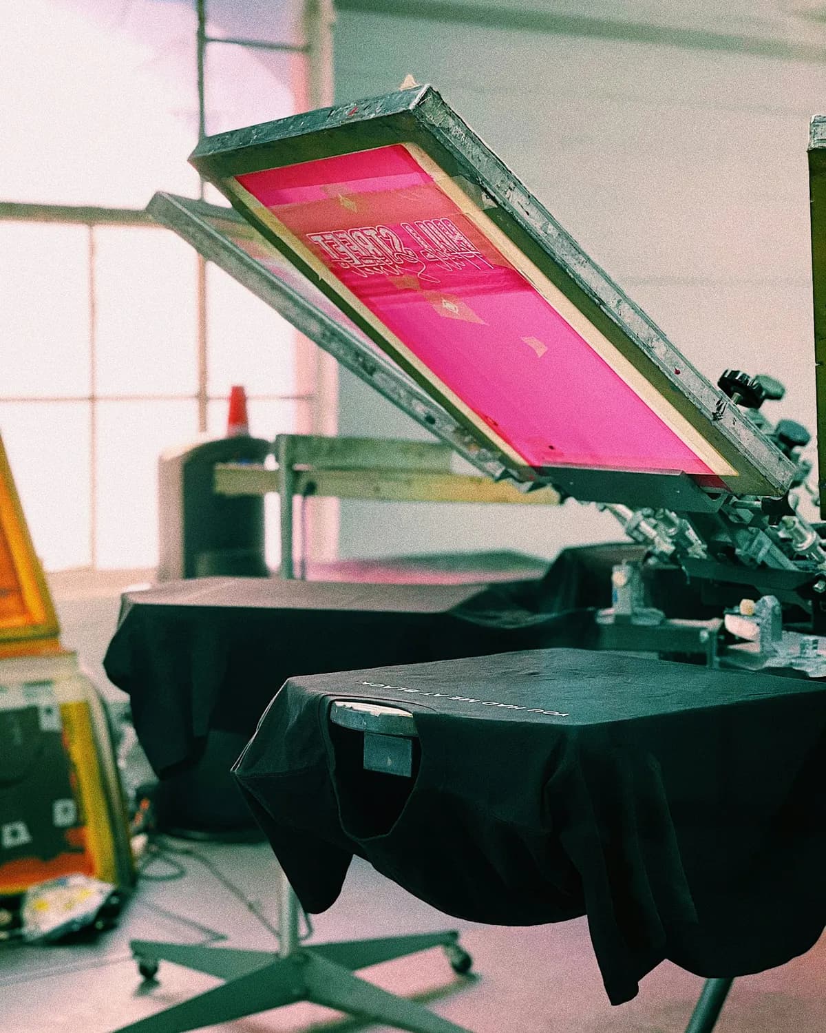 Carrousel de presse sérigraphie avec cadres rose et T-shirts noirs en attente d'impression.